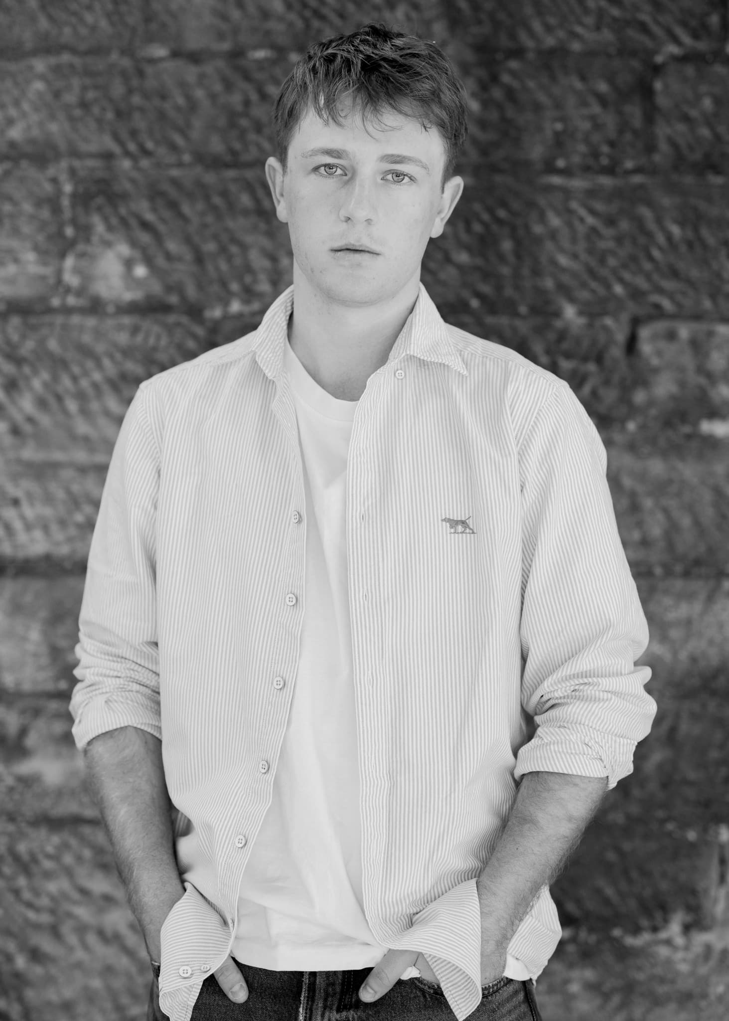Black and white portrait of a young man in a striped shirt against stone