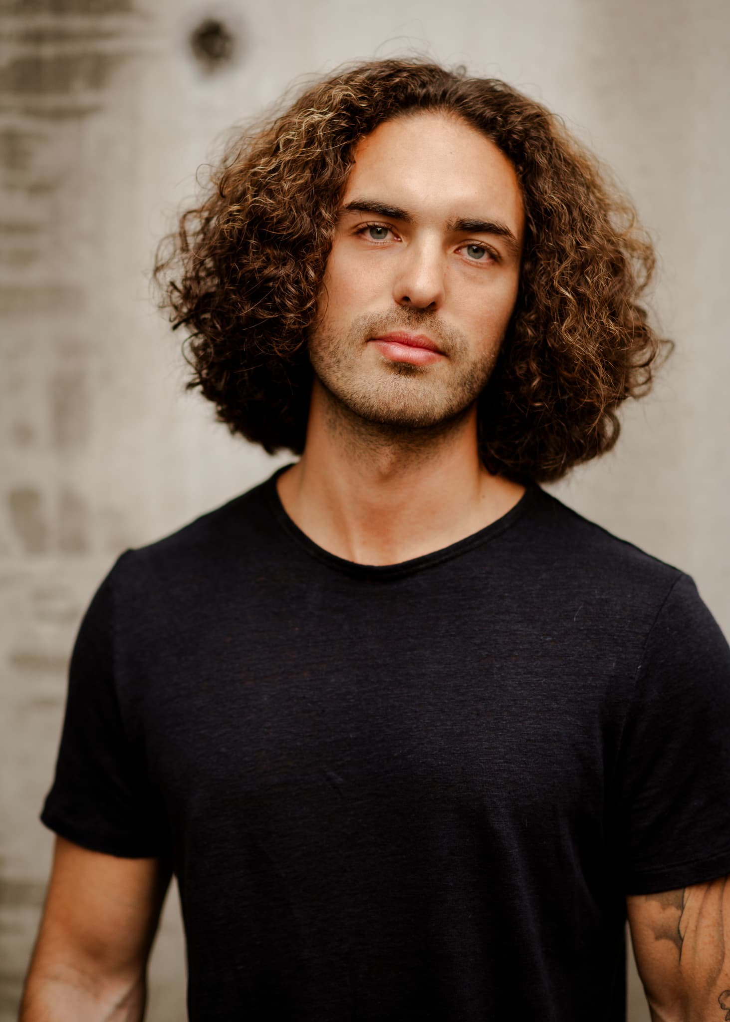 Portrait of a man with curly hair in a black tee, outdoors
