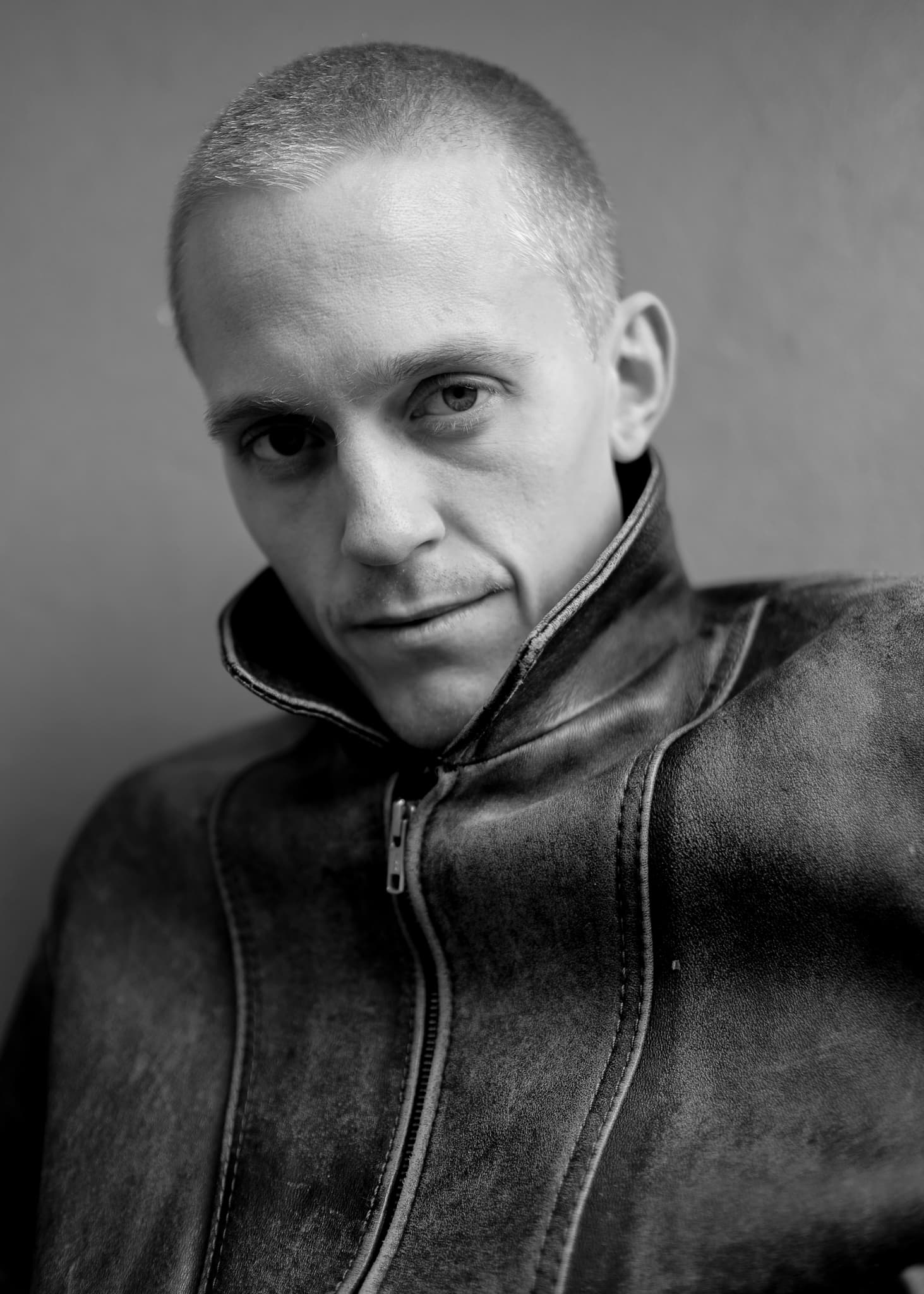 Black and white portrait of a man with a shaved head in a leather jacket